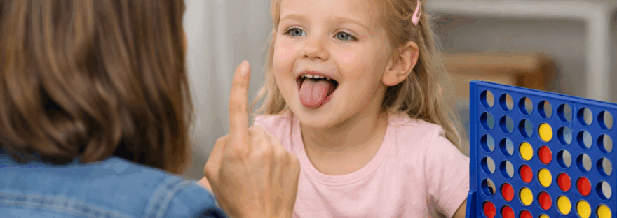 A young girl is learning how to put her tongue up for the 'l' sound in speech therapy.